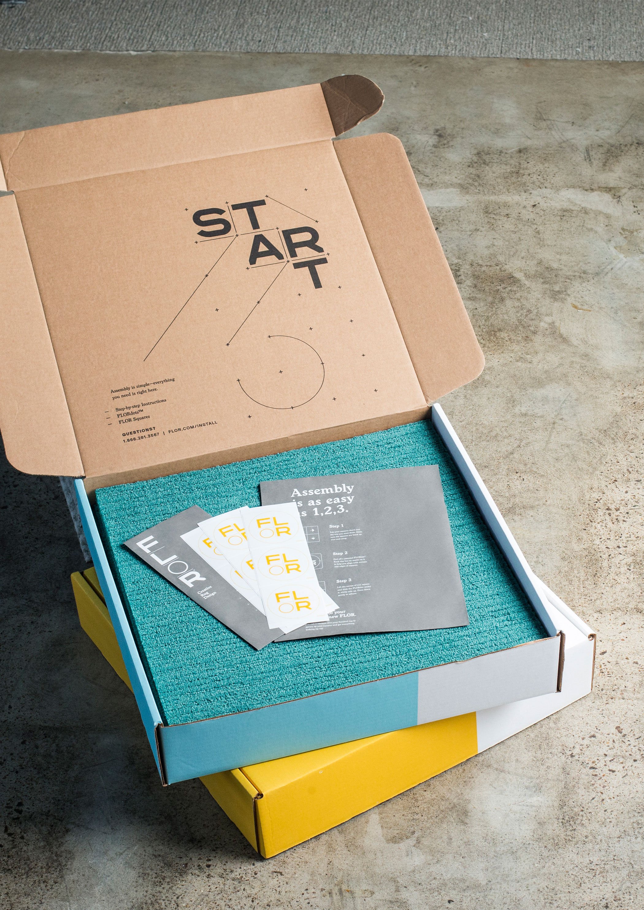 Open box of FLOR carpet tiles with FLORdots on top of a closed box of FLOR carpet tiles. 